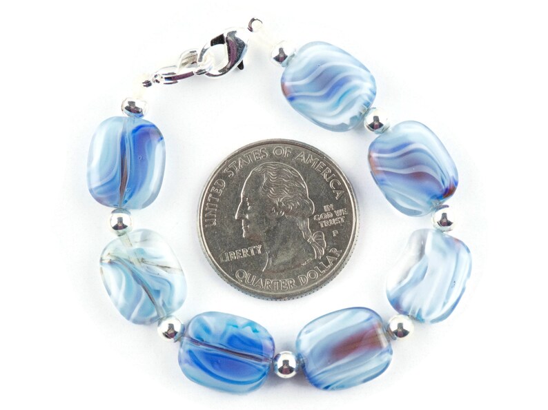 May include: A blue and white glass bead bracelet with a silver clasp. The bracelet is about the size of a quarter.