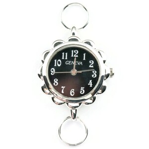 May include: A silver-toned watch with a black face and white numbers. The watch has a decorative, scalloped edge and is attached to a double ring.