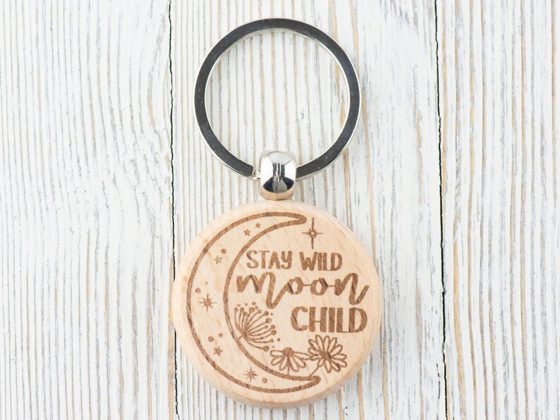 May include: Wooden keychain with a crescent moon design and the text "Stay Wild Moon Child".