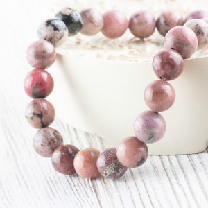 May include: A pink and gray gemstone bracelet with round beads. The bracelet is made of natural stones and is a beautiful accessory for any occasion.