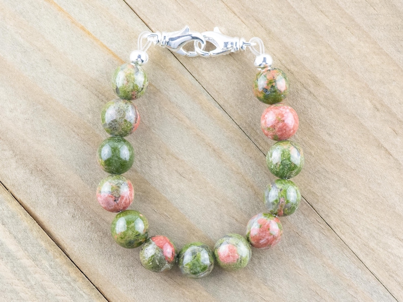 Puede incluir: Un brazalete de piedras preciosas verdes, rosas y blancas con un cierre plateado.