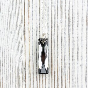 Pode incluir: Um colar de corrente de prata com um pingente de cristal preto retangular.