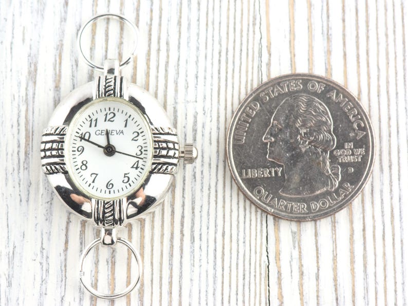 Pu&ograve; includere: Orologio Geneva argentato con quadrante bianco e numeri neri. L'orologio ha un quadrante rotondo e due anelli per il fissaggio. Una moneta &egrave; accanto all'orologio per il confronto delle dimensioni.