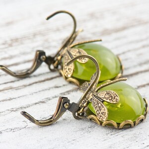 May include: A pair of green glass earrings with dragonfly accents. The earrings are made of brass and have a vintage style.