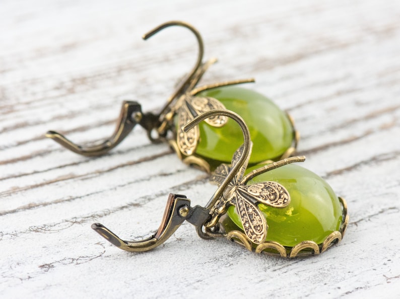 May include: A pair of green glass earrings with dragonfly accents. The earrings are made of brass and have a vintage style.