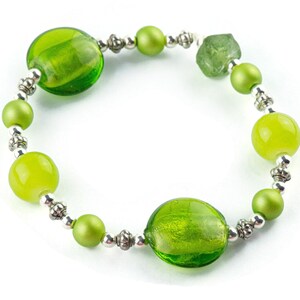 Puede incluir: Un brazalete de cuentas de vidrio verde con detalles plateados. El brazalete presenta cuentas redondas y ovaladas en varios tonos de verde.
