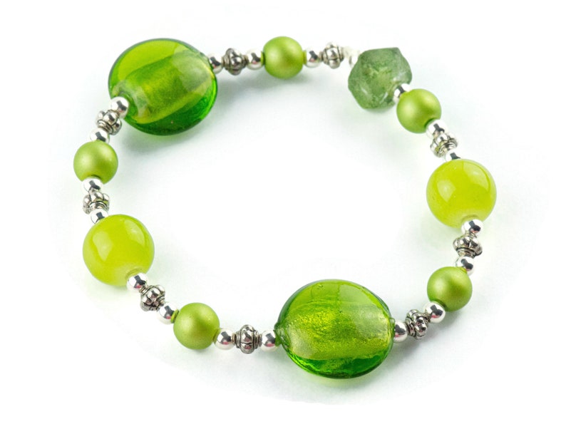 Puede incluir: Un brazalete de cuentas de vidrio verde con detalles plateados. El brazalete presenta cuentas redondas y ovaladas en varios tonos de verde.