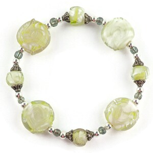 Peut inclure: Un bracelet en verre vert avec des motifs floraux grav&eacute;s et des accents argent&eacute;s.