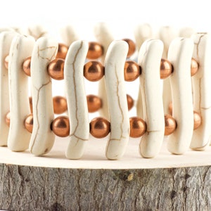 May include: A white and copper beaded bracelet with a woven design. The bracelet is made of white ceramic beads and copper beads.