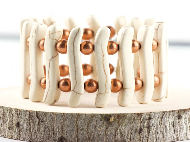 May include: A white and copper beaded bracelet with a woven design. The bracelet is made of white ceramic beads and copper beads.