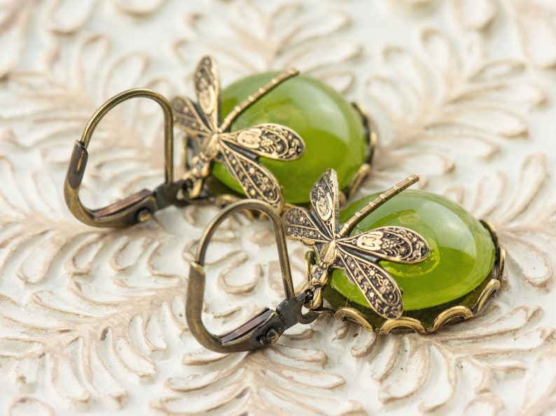 May include: A pair of green glass and bronze dragonfly earrings. The earrings feature a detailed dragonfly design with a green glass cabochon in the center.