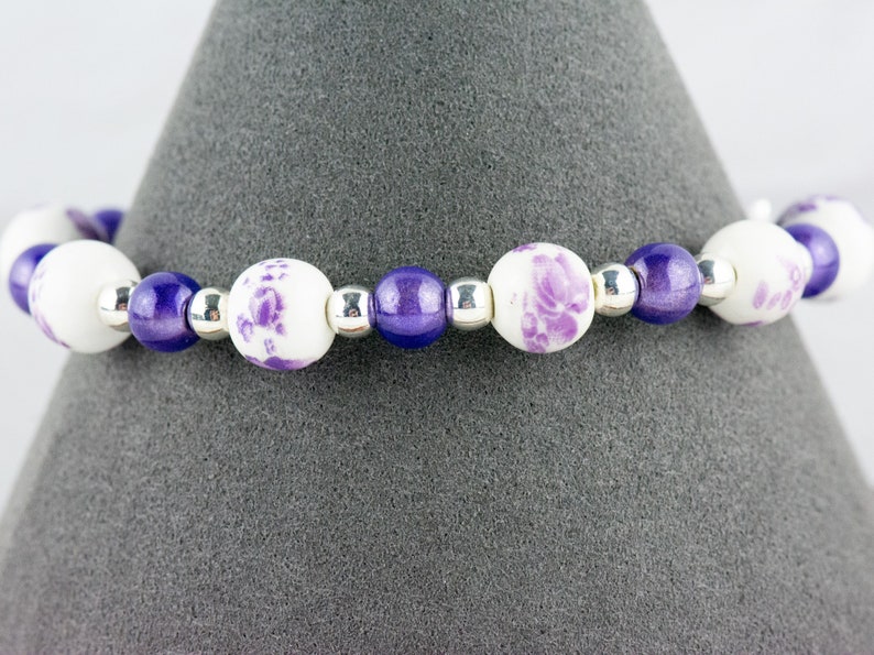 May include: A purple and white beaded bracelet with floral designs on the white beads.