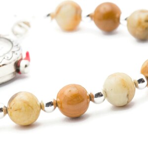 May include: A silver pocket watch with a white face and black hands is attached to a brown and white beaded bracelet.