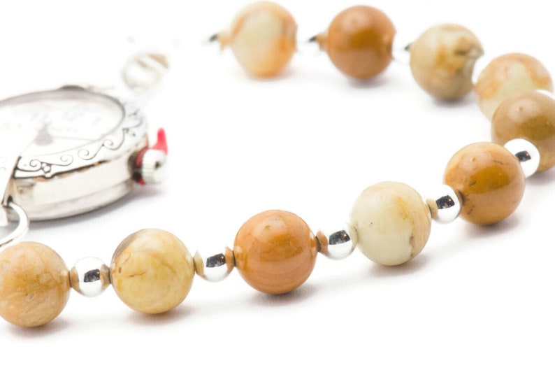 May include: A silver pocket watch with a white face and black hands is attached to a brown and white beaded bracelet.