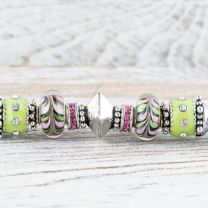 Peut inclure: Un bracelet &agrave; breloques argent&eacute; avec des perles en verre vertes et roses, un charme argent&eacute; et des entretoises argent&eacute;es.