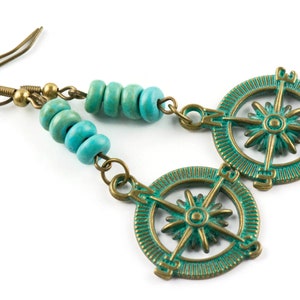 May include: Turquoise blue and bronze compass earrings with a beaded dangle. The compass features a starburst design with the cardinal directions marked.