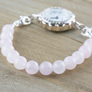 Puede incluir: Un reloj plateado con una esfera blanca y una pulsera de cuentas rosadas.