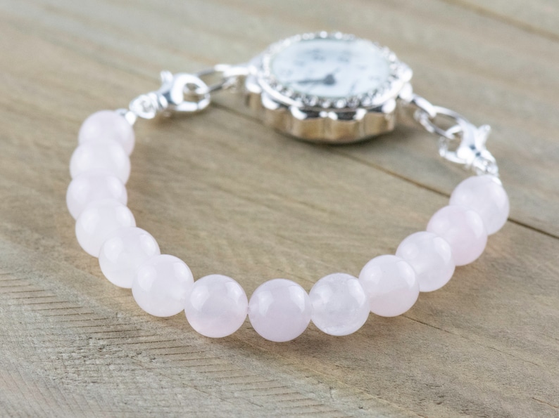 Puede incluir: Un reloj plateado con una esfera blanca y una pulsera de cuentas rosadas.
