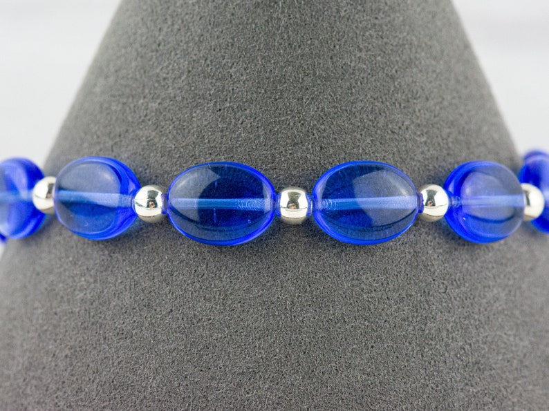 May include: A blue glass bead bracelet with silver spacer beads. The bracelet is on a gray background.