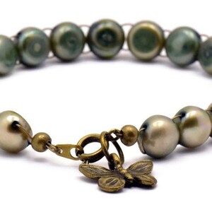Op de afbeelding: Een armband gemaakt van groene en witte parels met een bronzen vlinderbedel.