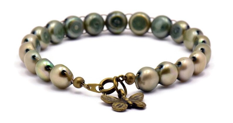 Op de afbeelding: Een armband gemaakt van groene en witte parels met een bronzen vlinderbedel.