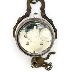 May include: A vintage-style pocket watch with a clear back revealing the inner workings of the mechanism. The watch has a brass finish and a chain attached.