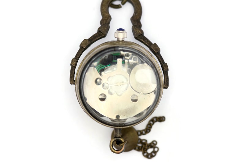 May include: A vintage-style pocket watch with a clear back revealing the inner workings of the mechanism. The watch has a brass finish and a chain attached.