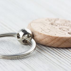 May include: A wooden keyring with a silver ring. The wood is light brown and has a design engraved on it.