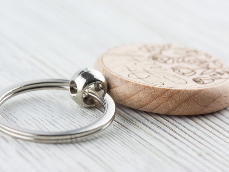 May include: A wooden keyring with a silver ring. The wood is light brown and has a design engraved on it.