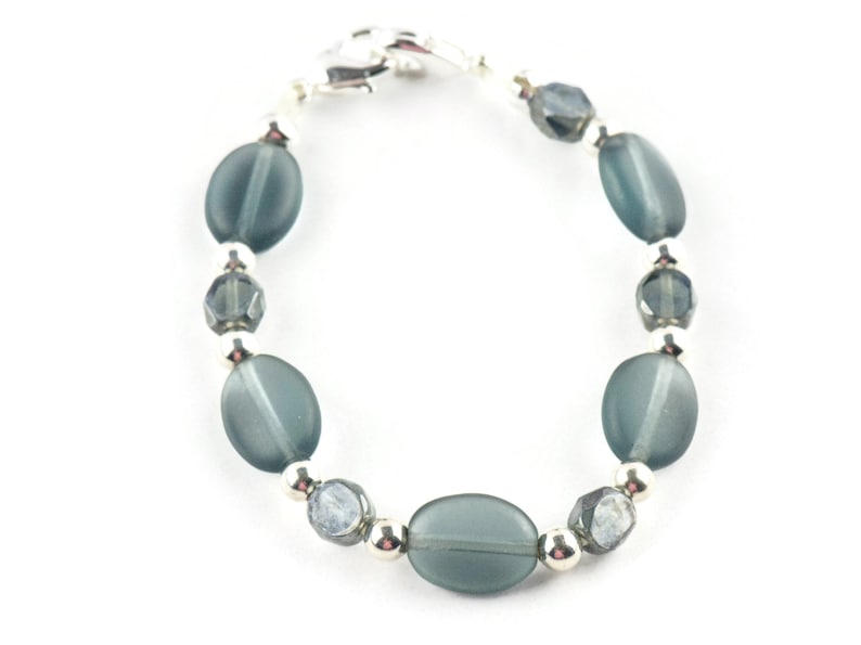 Pu&ograve; includere: Un braccialetto con perline ovali e sfaccettate nei toni del verde acqua e grigio, intervallate da piccole perline color argento. Il braccialetto &egrave; assicurato con una chiusura argentata, che mostra un design delicato ed elegante.