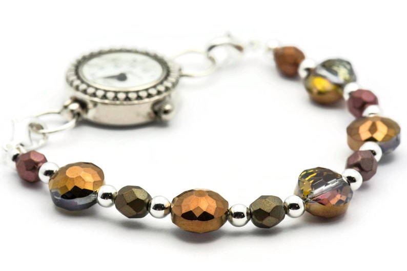 K&ouml;nnte beinhalten: Eine silberne Uhr mit wei&szlig;em Zifferblatt und schwarzen Zeigern, die an einem Armband mit braunen, goldenen und silbernen Perlen befestigt ist.