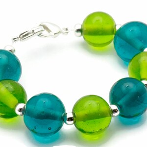 Puede incluir: Un brazalete hecho de cuentas de vidrio alternas de color verde azulado y verde lima con separadores plateados.