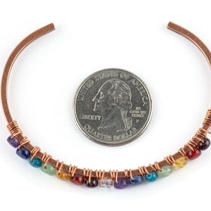 K&ouml;nnte beinhalten: Kupferdraht-Armband mit einem Regenbogen aus Edelsteinen, darunter Amethyst, Lapislazuli, T&uuml;rkis, gr&uuml;ner Aventurin, Citrin, Karneol, roter Jaspis und klarer Quarz. Das Armband ist neben einer 20-Cent-M&uuml;nze zur Gr&ouml;&szlig;enreferenz abgebildet.