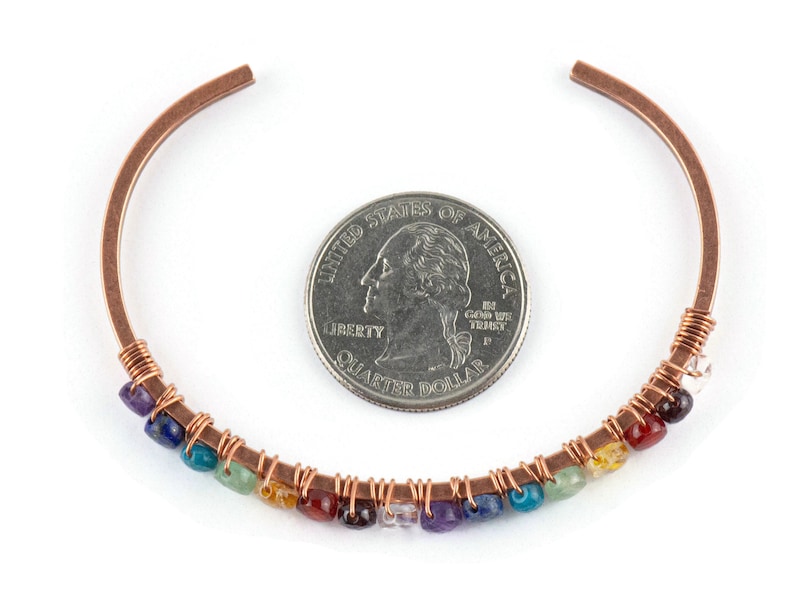 K&ouml;nnte beinhalten: Kupferdraht-Armband mit einem Regenbogen aus Edelsteinen, darunter Amethyst, Lapislazuli, T&uuml;rkis, gr&uuml;ner Aventurin, Citrin, Karneol, roter Jaspis und klarer Quarz. Das Armband ist neben einer 20-Cent-M&uuml;nze zur Gr&ouml;&szlig;enreferenz abgebildet.