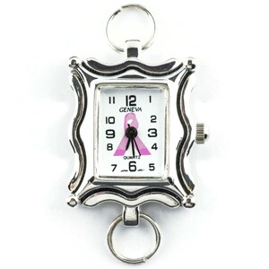 K&ouml;nnte beinhalten: Silberfarbene Geneva-Quarzuhr mit rechteckigem Zifferblatt und rosa Schleifendesign. Die Uhr hat einen dekorativen Rahmen und zwei Schl&uuml;sselringe. Das Zifferblatt zeigt die Uhrzeit und das Wort "GENEVA".