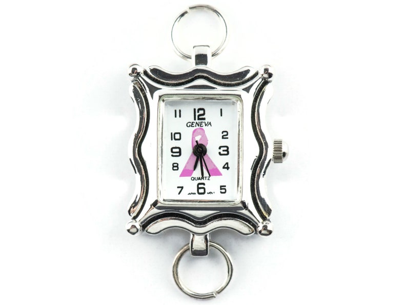 K&ouml;nnte beinhalten: Silberfarbene Geneva-Quarzuhr mit rechteckigem Zifferblatt und rosa Schleifendesign. Die Uhr hat einen dekorativen Rahmen und zwei Schl&uuml;sselringe. Das Zifferblatt zeigt die Uhrzeit und das Wort "GENEVA".