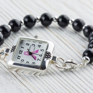 Pu&ograve; includere: Orologio argentato con quadrante quadrato e bracciale di perline nere. Il quadrante dell'orologio presenta un nastro rosa e il bracciale &egrave; composto da grandi perline nere rotonde. L'orologio &egrave; collegato al bracciale con chiusure argentate.