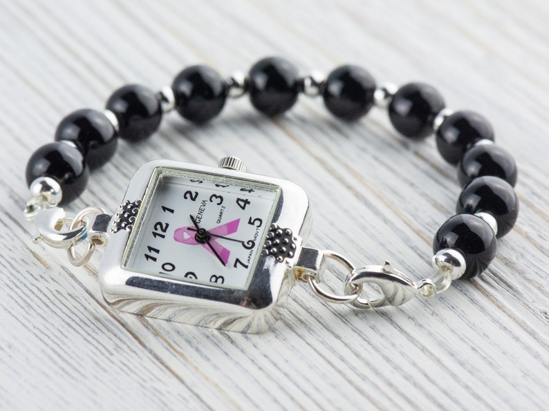 Pu&ograve; includere: Orologio argentato con quadrante quadrato e bracciale di perline nere. Il quadrante dell'orologio presenta un nastro rosa e il bracciale &egrave; composto da grandi perline nere rotonde. L'orologio &egrave; collegato al bracciale con chiusure argentate.