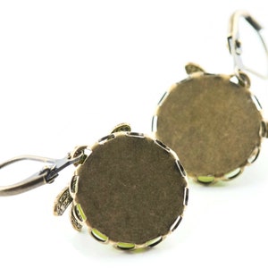 May include: A pair of gold-tone earrings with a round, green stone set in a decorative frame. The earrings have a lever-back closure.