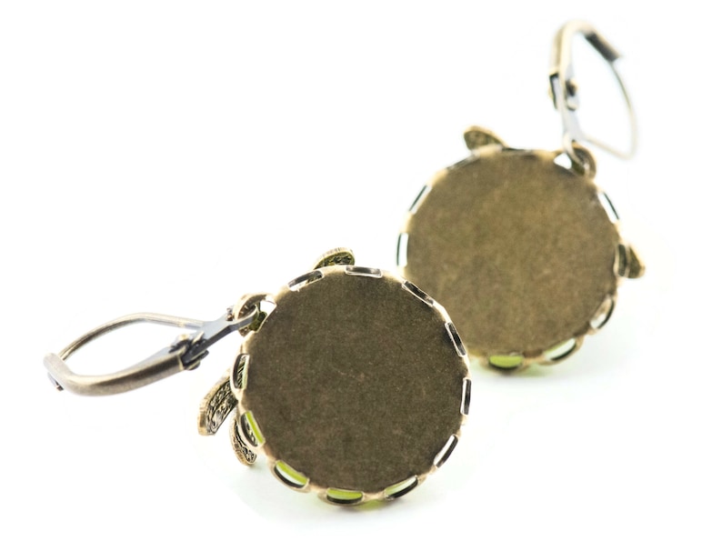May include: A pair of gold-tone earrings with a round, green stone set in a decorative frame. The earrings have a lever-back closure.