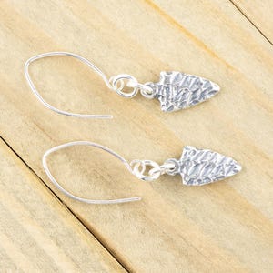 K&ouml;nnte beinhalten: Ein Paar silberne Ohrringe mit einem strukturierten Pfeilspitzen-Design. Die Ohrringe sind aus Sterlingsilber gefertigt und haben ein schlichtes, elegantes Design.
