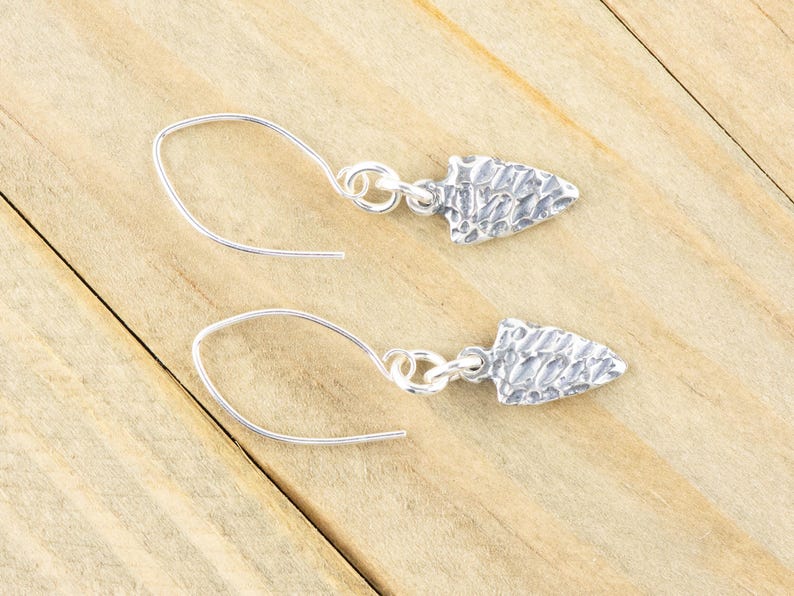 K&ouml;nnte beinhalten: Ein Paar silberne Ohrringe mit einem strukturierten Pfeilspitzen-Design. Die Ohrringe sind aus Sterlingsilber gefertigt und haben ein schlichtes, elegantes Design.