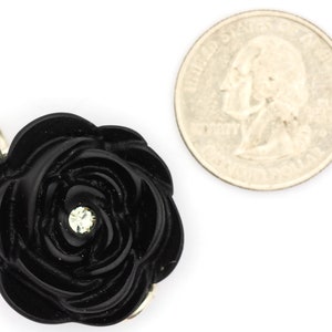 May include: A black resin rose with a single rhinestone in the center. The rose is about the size of a US quarter.