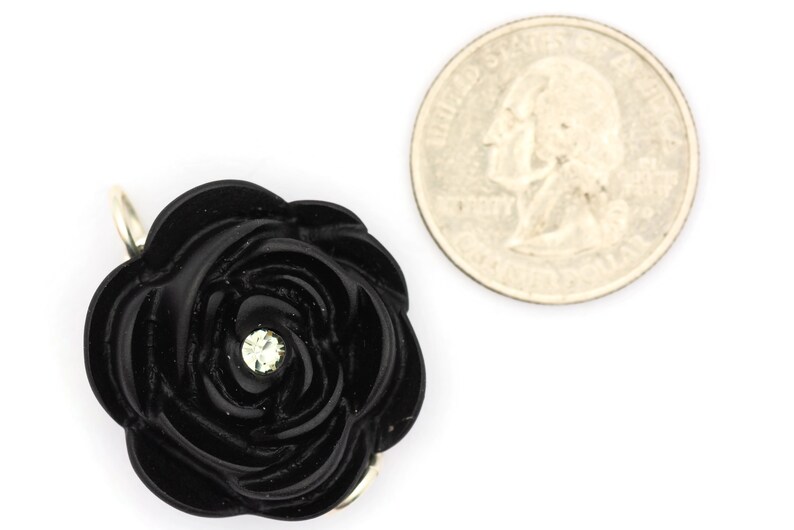 May include: A black resin rose with a single rhinestone in the center. The rose is about the size of a US quarter.