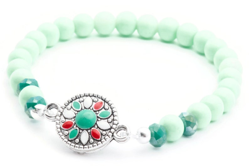 May include: A mint green beaded bracelet with a silver charm featuring a green, red and white floral design.