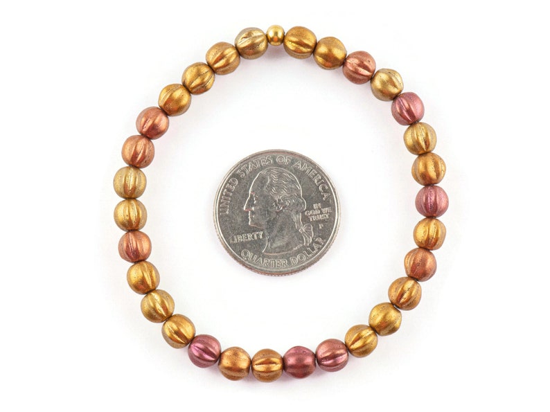 May include: A gold and copper toned beaded bracelet with a textured finish. The bracelet is approximately the size of a US quarter.