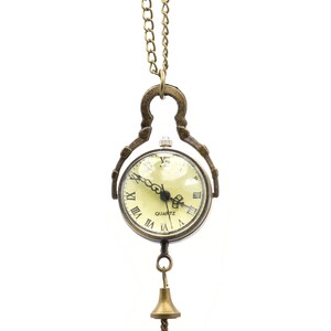 May include: A gold-toned pocket watch necklace with Roman numeral markings on the face. The watch has a quartz movement and is attached to a delicate chain with a bell-shaped pendant.