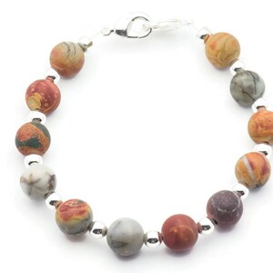 May include: A beaded bracelet featuring round, multicolored stone beads in shades of red, brown, gray, and cream. The beads are separated by small, silver-colored beads and connected with a silver clasp.