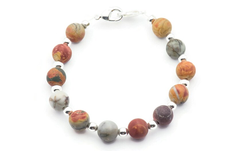 May include: A beaded bracelet featuring round, multicolored stone beads in shades of red, brown, gray, and cream. The beads are separated by small, silver-colored beads and connected with a silver clasp.