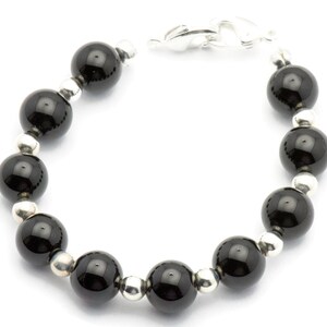 Puede incluir: Una pulsera con grandes cuentas negras brillantes intercaladas con cuentas m&aacute;s peque&ntilde;as de color plateado. La pulsera se asegura con un cierre plateado. Las cuentas est&aacute;n espaciadas uniformemente, creando un dise&ntilde;o simple pero elegante.